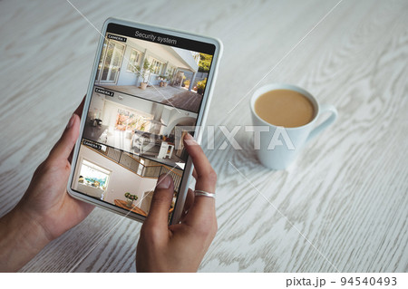 Hands of african american woman holding tablet with view of home from security cameras on screen 94540493