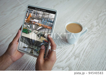 Hands of african american woman using tablet with view of warehouse from security cameras on screen 94540583