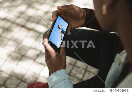African american man in park watching male athlete throwing discus on smartphone African american man in park watching male athlete throwing discus on smartphone 94540648