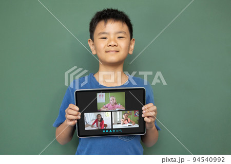Smiling asian boy holding tablet for video call, with diverse elementary school pupils on screen Smiling asian boy holding tablet for video call, with diverse elementary school pupils on screen 94540992