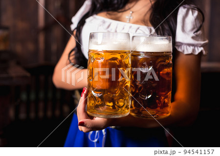 Young sexy Oktoberfest waitress, wearing a traditional Bavarian dress, serving big beer mugs at bar. 94541157