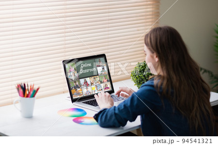 Caucasian woman using laptop for video call, with diverse elementary school pupils on screen 94541321