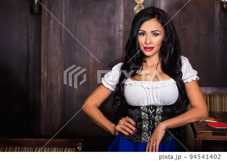 Oktoberfest woman wearing a traditional Bavarian dress dirndl posing at bar 94541402