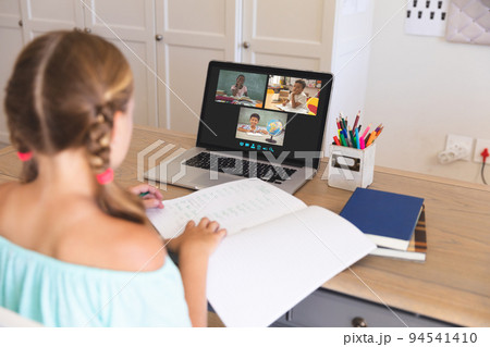 Caucasian girl using laptop for video call, with diverse elementary school pupils on screen 94541410