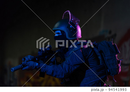 Army soldier in Combat Uniforms with an assault rifle and combat helmet night mission dark background. Blue and purple gel light effect. Army soldier in Combat Uniforms with an assault rifle and combat helmet night mission dark background. Blue and purple gel light effect. 94541993
