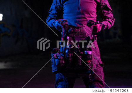 Army soldier in Combat Uniforms with an assault rifle and combat helmet night mission dark background. Blue and purple gel light effect.  94542003