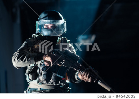 Army soldier in Combat Uniforms with an assault rifle and combat helmet night mission dark background. Blue and purple gel light effect.  94542005