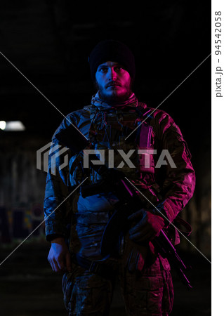 Army soldier in Combat Uniforms with an assault rifle and combat helmet night mission dark background. Blue and purple gel light effect. Army soldier in Combat Uniforms with an assault rifle and combat helmet night mission dark background. Blue and purple gel light effect. 94542058