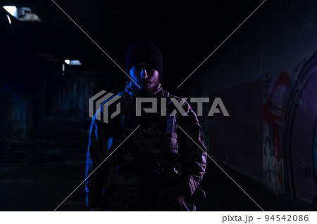 Army soldier in Combat Uniforms with an assault rifle and combat helmet night mission dark background. Blue and purple gel light effect. Army soldier in Combat Uniforms with an assault rifle and combat helmet night mission dark background. Blue and purple gel light effect. 94542086