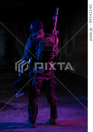 Army soldier in Combat Uniforms with an assault rifle and combat helmet night mission dark background. Blue and purple gel light effect.  94542140