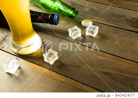 Image of beer bottles, ice cubes and pint glass of beer on wooden table, with copy space 94542477