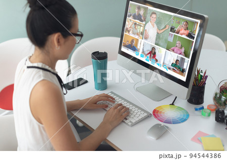 Asian girl holding computer for video call, with smiling diverse elementary school pupils on screen 94544386