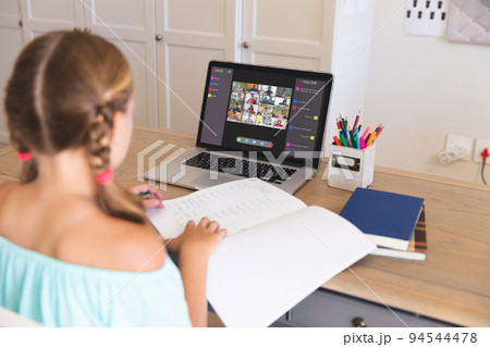 Caucasian girl using laptop for video call, with diverse elementary school pupils on screen 94544478