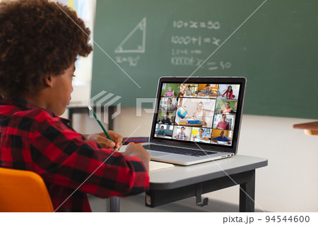 African american boy using laptop for video call, with diverse elementary school pupils on screen 94544600