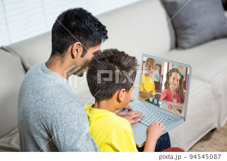 Biracial boy with father using laptop for video call, with elementary school pupils on screen 94545087