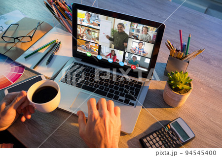 Hands of man using laptop for video call, with smiling diverse elementary school pupils on screen Hands of man using laptop for video call, with smiling diverse elementary school pupils on screen 94545400