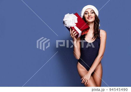 Portrait of young, sexy and beautiful woman in swimsuit and Santa hat, holding gift box. Girl in underwear lingerie. Blue background. Christmas, xmas, x-mas and winter concept 94545490