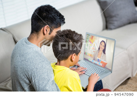 Biracial boy with father using laptop for video call, with smiling caucasian teacher on screen 94547090