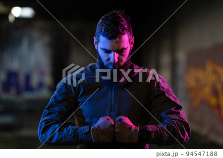 Photo of a fully equipped soldier in black armor tactical vest and gloves standing on black background closeup front view. Photo of a fully equipped soldier in black armor tactical vest and gloves standing on black background closeup front view. 94547188