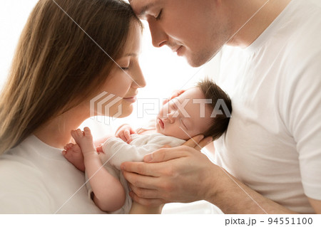 Close up portrait of young parents and newborn baby. Father and mother kiss and hug a beautiful newborn daughter. The concept of love, happy fatherhood and motherhood. Photography on white background. 94551100