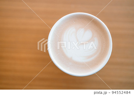 Paper cup of cappuccino coffee with latte art on wooden table in cafe. Flat lay, top view  94552484