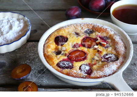Damson blue plum clafoutis (flan) and cup of tea, icing sugar and almonds dressing 94552666