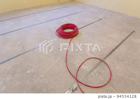 Heating red electrical cable wire roll on cement floor copy space background. Renovation and construction, comfortable warm home concept. Heating red electrical cable wire roll on cement floor copy space background. Renovation and construction, comfortable warm home concept. 94554128