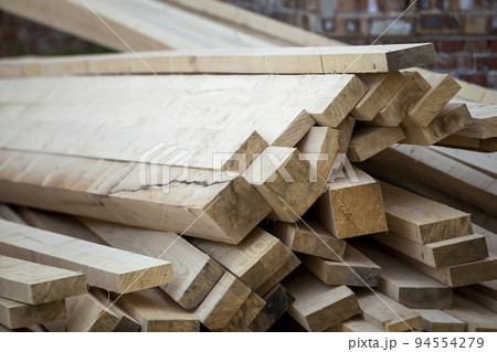 Close-up of piled stack of natural brown uneven rough wooden boards lit by bright sun. Industrial timber for carpentry, building, repairing and furniture, lumber material for construction. 94554279