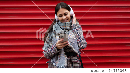 portrait of a young woman student in headphones with a mobile phone against the background of a red 94555043
