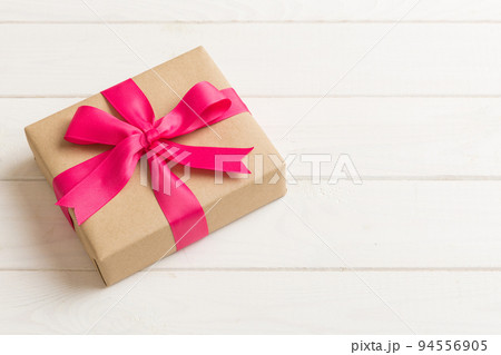 Wrapped christmas or other holiday handmade present in craft paper with colored ribbon. Present box, decoration of gift on table, top view with copy space 94556905