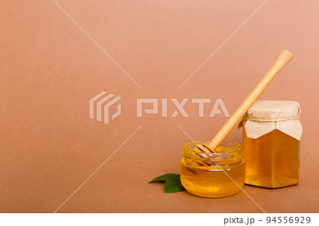 Honey in jar with leaves and honey dipper on colored background top view with copy text 94556929