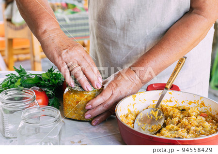 Woman pickles, ferments salad vegetables for preservation in jars zucchini eggplant tomatoes herbs 94558429