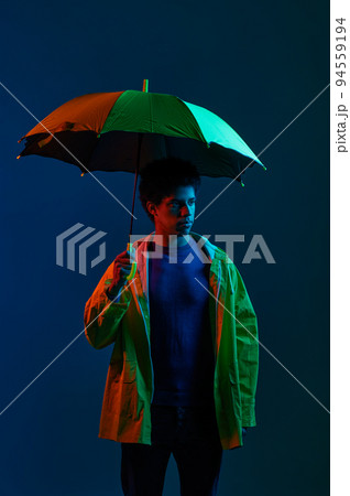 Man in raincoat under umbrella over dark studio background 94559194