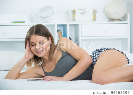 Portrait of young sexy woman lying with smartphone in bed Portrait of young sexy woman lying with smartphone in bed 94562597