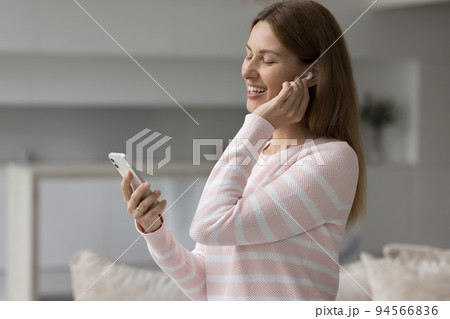Happy woman with wireless earphone in ear listening to music Happy woman with wireless earphone in ear listening to music 94566836