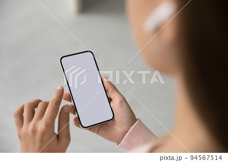 Millennial woman with wireless earphone in ear using mobile phone 94567514