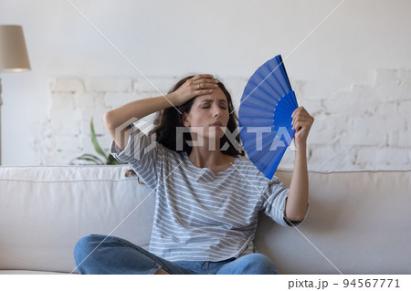 Overheated Hispanic woman wave fan, cooling herself at hot day 94567771