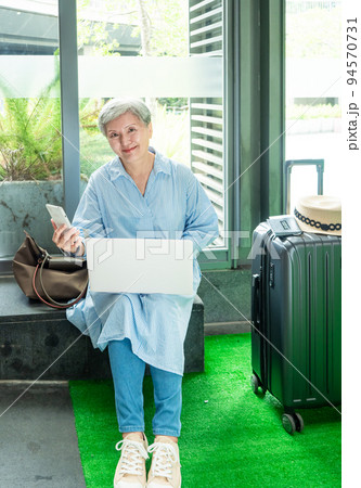 relax, vacation, travel, portrait of senior adult elderly asian woman 60s smiling using the computer laptop and smartphone while waiting for their travel time. relax, vacation, travel, portrait of senior adult elderly asian woman 60s smiling using the computer laptop and smartphone while waiting for their travel time. 94570731