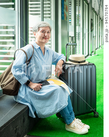 relax, vacation, travel, portrait of senior adult elderly asian woman 60s smiling sitting with suitcase luggage bag while waiting for her travel time. relax, vacation, travel, portrait of senior adult elderly asian woman 60s smiling sitting with suitcase luggage bag while waiting for her travel time. 94570764