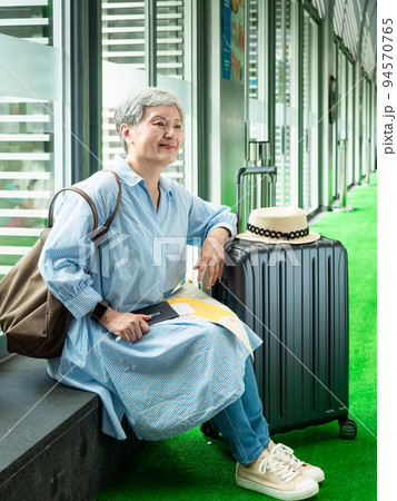relax, vacation, travel, portrait of senior adult elderly asian woman 60s smiling sitting with suitcase luggage bag while waiting for her travel time. 94570765