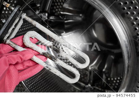 A man holds in his hand a burnt-out heating element of a washing machine against the background of a washing machine drum A man holds in his hand a burnt-out heating element of a washing machine against the background of a washing machine drum 94574455