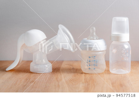 Manual breast pump and nursing bottles for newborn baby on wooden table. Device for increasing milk supply for breastfeeding mother. Maternity, baby care concept. Manual breast pump and nursing bottles for newborn baby on wooden table. Device for increasing milk supply for breastfeeding mother. Maternity, baby care concept. 94577518
