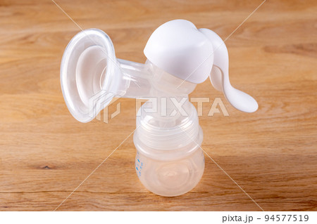 Manual breast pump on wooden table. Device for increasing milk supply for breastfeeding mother. Maternity and baby care concept 94577519