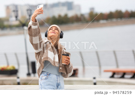 Photo of a young woman taking a selfie with her smartphone during outdoor walk. Photo of a young woman taking a selfie with her smartphone during outdoor walk. 94578259