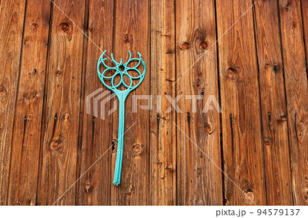 broken plastic carpet beater hanging on a nail on a wooden wall 94579137