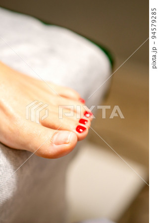 Nail painting process. Red painted fingernails on a female leg in a beauty salon, closeup Nail painting process. Red painted fingernails on a female leg in a beauty salon, closeup 94579285