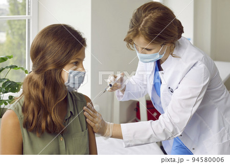 Female nurse or doctor in medical face mask giving vaccine injection to child patient 94580006