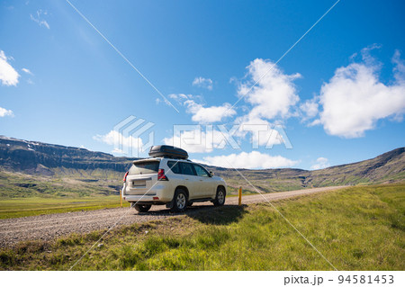 Large car parked on dirt road among the mountain and meadow on sunny day in summer Large car parked on dirt road among the mountain and meadow on sunny day in summer 94581453