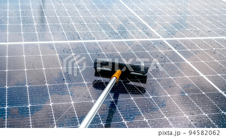Cleaning solar panel with microfiber mop on wet roof. Solar panel or photovoltaic module maintenance service. Sustainable resource. Solar power. Green energy. Sustainable development technology. 94582062