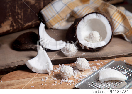 Close up of coconut with white pulp, grater with coconut chip and white candies on wooden background.. Close up of coconut with white pulp, grater with coconut chip and white candies on wooden background.. 94582724